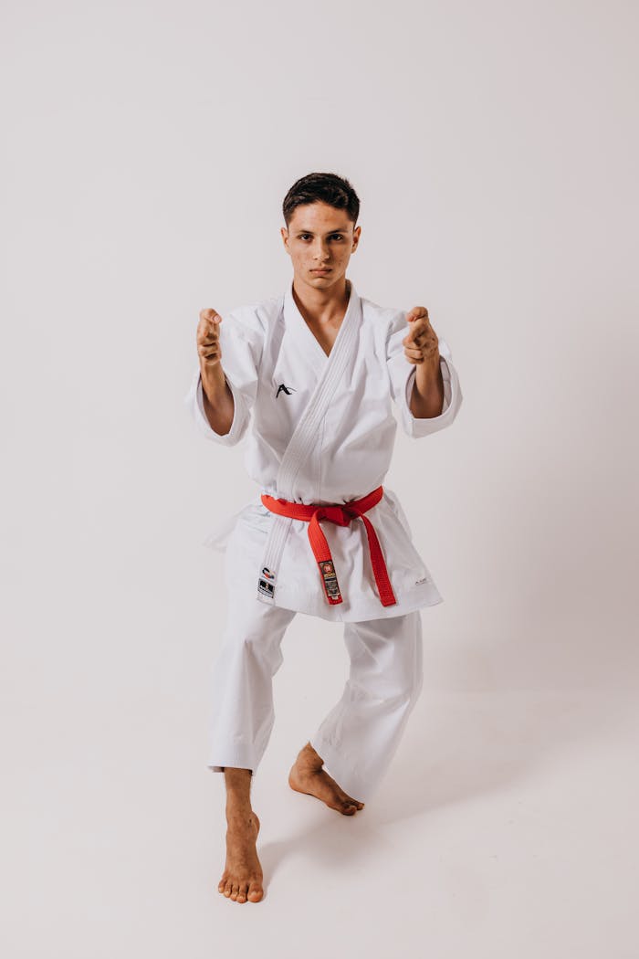Teen karate athlete in white kimono with red belt poses confidently in studio setting.